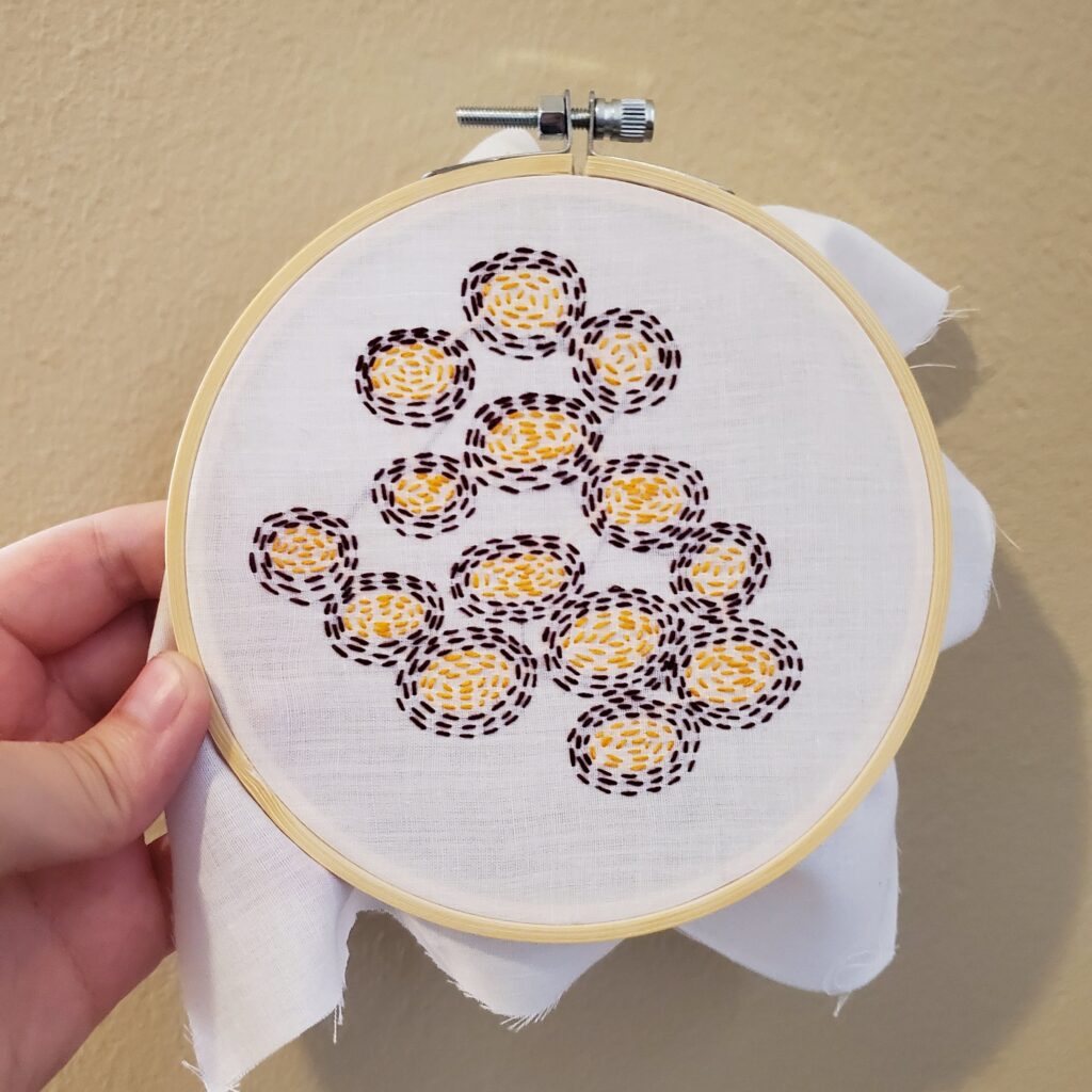 Embroidery hoop with outwarding expanding embroidered circles. the insides are yellow and then dark red.