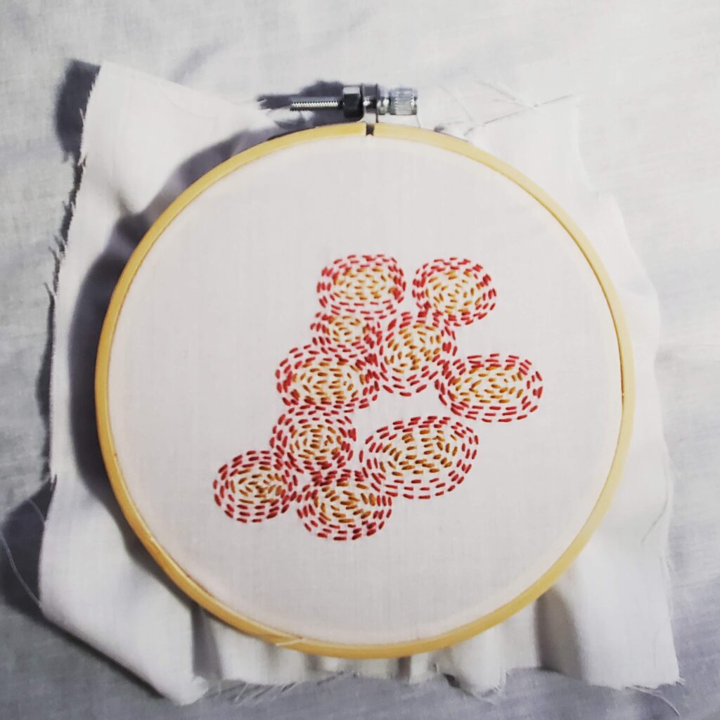 Embroidery hoop with outwarding expanding embroidered circles. the insides are yellow and then red.