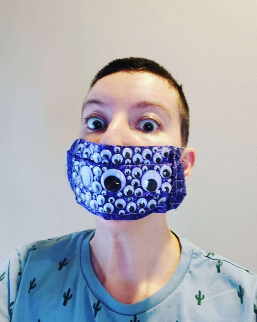 Young woman wearing purple mask with different-sized googly eyes on it.
