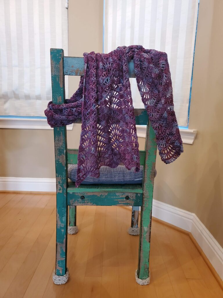 Purple hand knitted scarf draped on back of green chair.