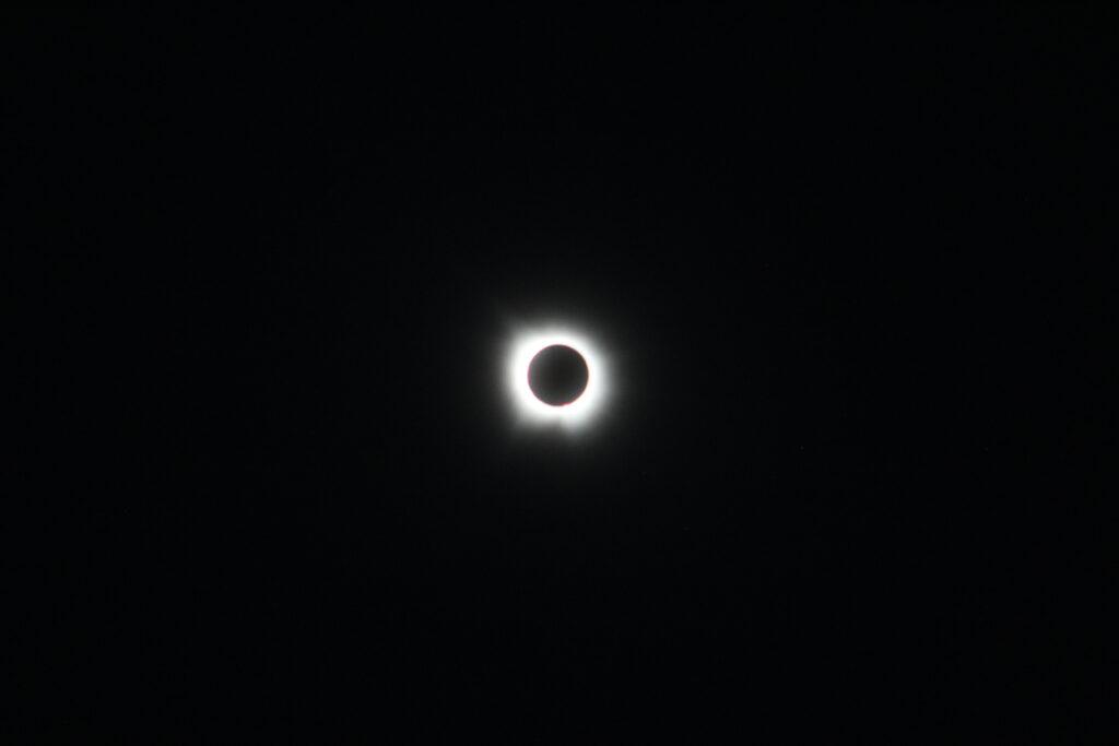 Photo of total solar eclipse. Moon is black in front of white rays from Sun.